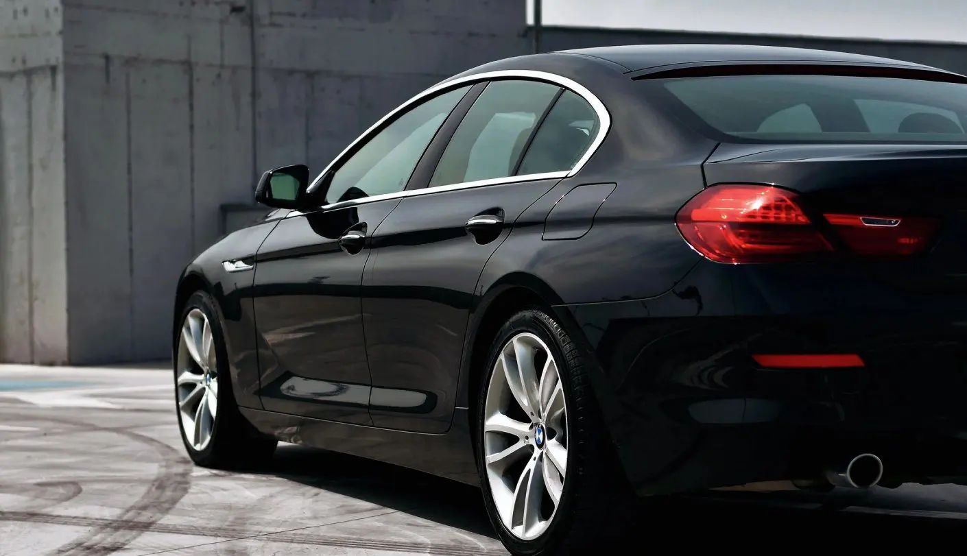 A black car parked in the street next to a wall.