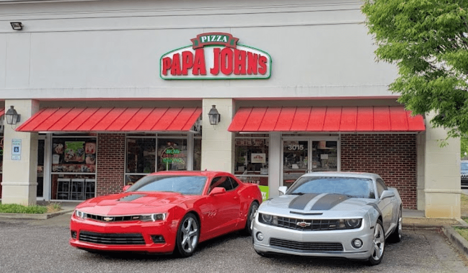 Two red and white cars parked in front of a pizza joint.