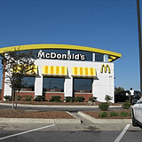 A mcdonald 's restaurant with yellow awnings and a car parked in front.