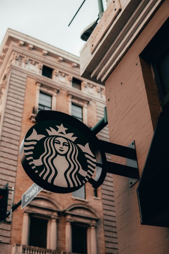 A starbucks sign hanging from the side of a building.