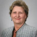 Professional headshot of a smiling woman in a gray blazer.