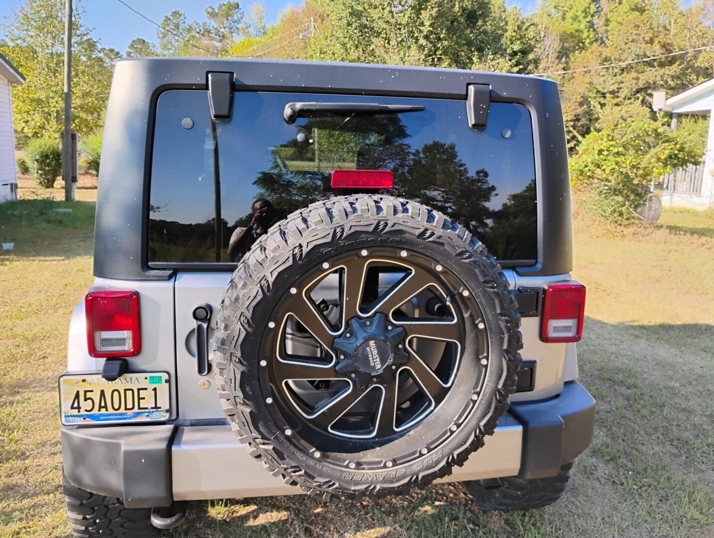 Spare tire mounted on the back of a white Jeep with rugged off-road tires.