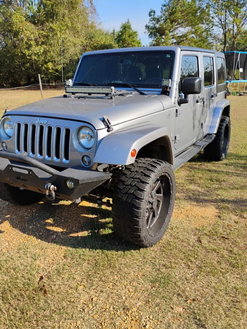 White Jeep Wrangler parked on grass with large off-road tires.