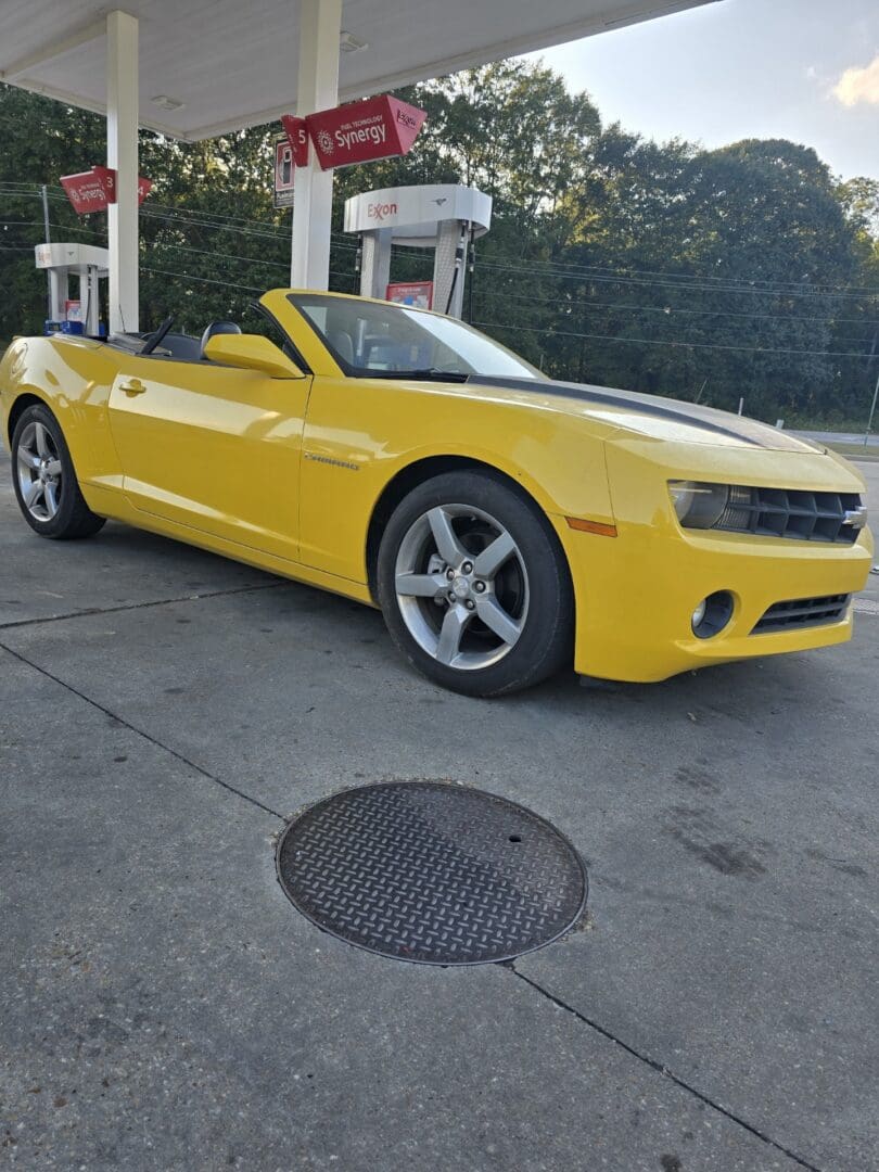 Yellow convertible sports car parked near a gas station.