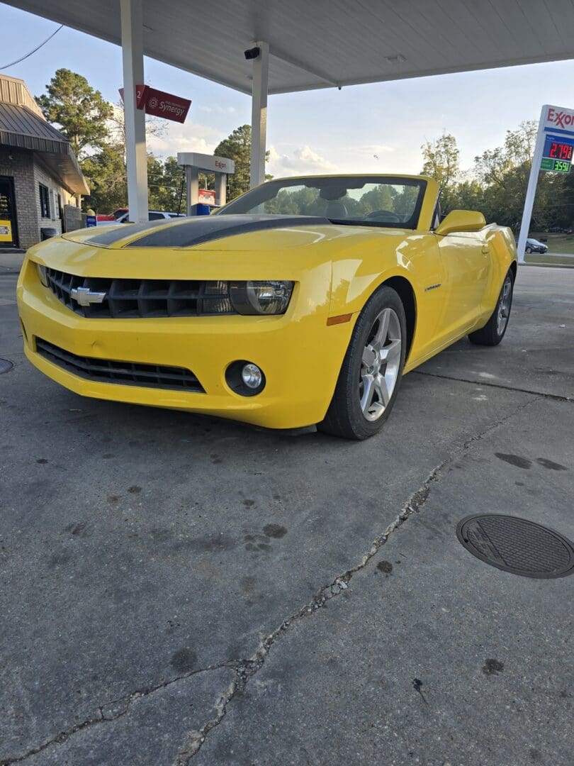 Yellow Chevrolet Camaro parked at a gas station during sunset.