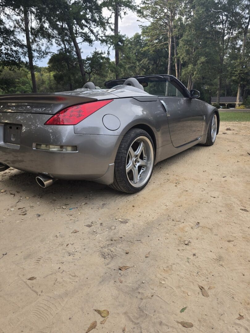 A sleek silver sports car parked on a dirt patch.