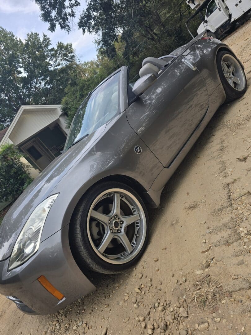 Silver sports car parked on a driveway under trees.