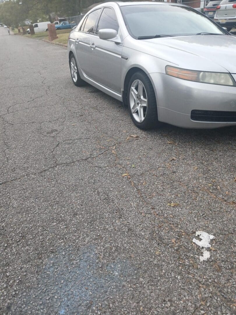 Silver car parked on a rough asphalt surface with a small white object nearby.