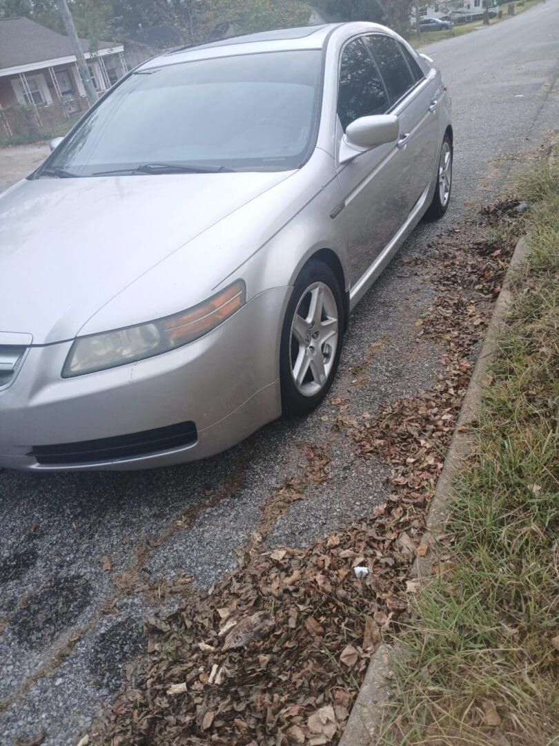 Silver car parked partially on the road and grass beside a curb.