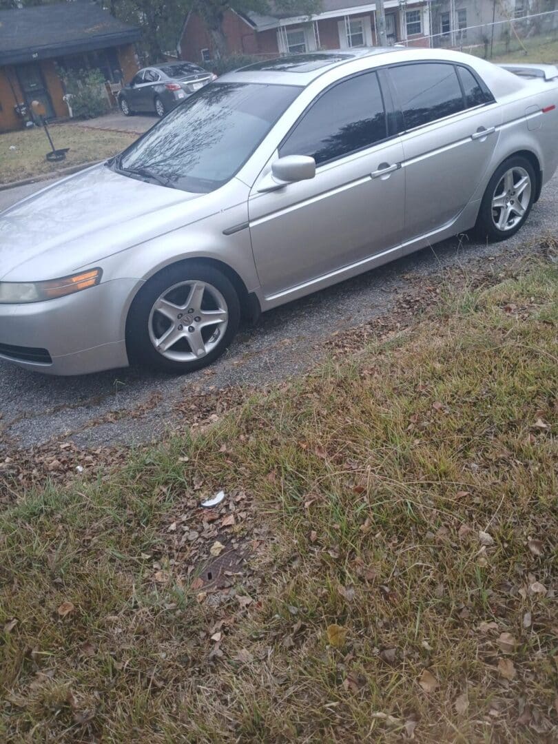Silver sedan parked on a narrow road beside a grassy area.