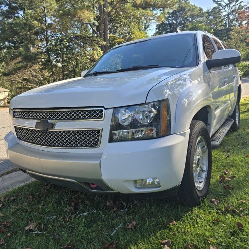 White Chevrolet SUV parked on grass near trees.