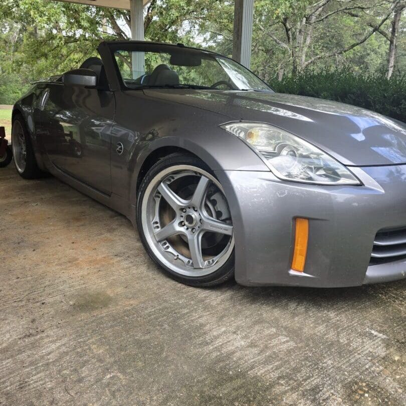Sleek silver sports car parked under a tree on a driveway.